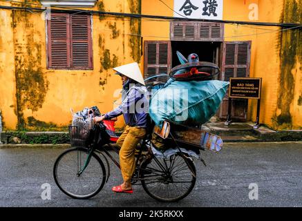 A female cyclist rides a bike along the road in the old town of Hoi An, Vietnam. Stock Photo