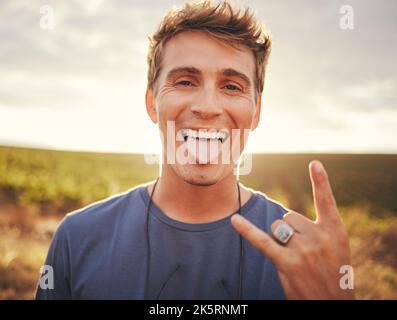Man, hands and portrait of rock sign for travel tour or vacation in the countryside and nature outdoors. Happy, excited young male traveler, rocker or Stock Photo