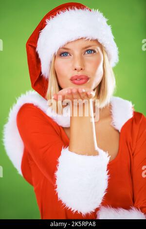 Wishing you a wonderful Christmas. Portrait of beautiful young female blowing a kiss on a green background - Christmas. Stock Photo