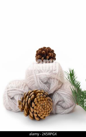 Balls of gray wool yarn with cones and spruce branch on white background. Knitting, needlework. Copy space Stock Photo