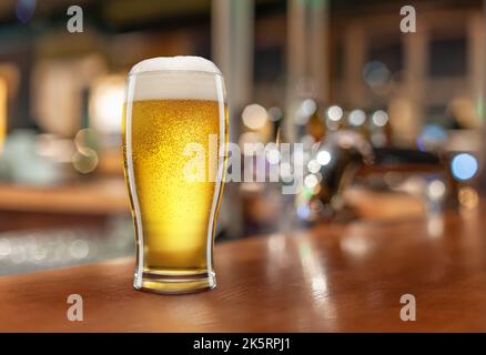 Glass with light beer on a wooden table against the backdrop of a dark pub. Beer vintage concept. Stock Photo