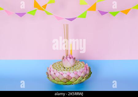 Pink lotus petal krathong that have 3 incense sticks and candle decorates with lotus and crown flower for Thailand Loy Krathong festival on pink and b Stock Photo