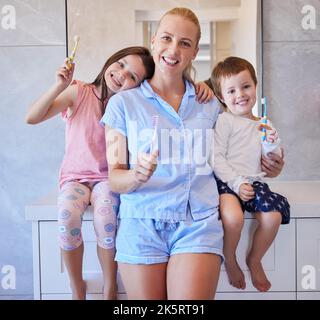 Portrait of happy young caucasian family holding toothbrushes and smiling showing off their healthy teeth. Young mother and her two children getting Stock Photo