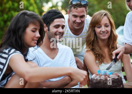 Ready to share the birthday cake. Happy young teen friends celebrating someones birthday and cutting some birthday cake. Stock Photo