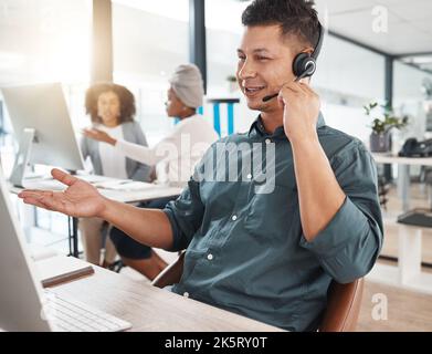 Happy hispanic call centre telemarketing agent talking on a headset while working on a computer in an office. Confident friendly male consultant Stock Photo