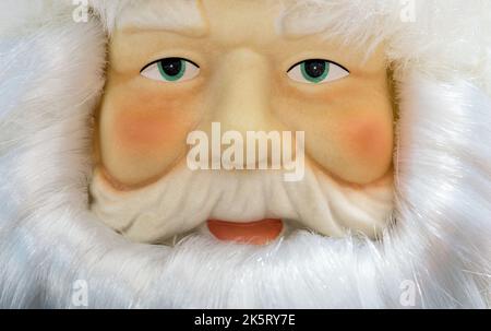 Santa Claus decorative doll closeup with facial features and details, looking at camera. Framed by white beard and hair. Stock Photo