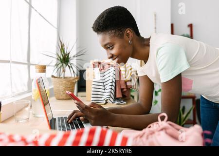 Small business african owner woman with mobile phone working on laptop in office Stock Photo