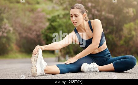 One fit young mixed race woman touching her feet and stretching legs for warmup to prevent injury while exercising outdoors. Female athlete preparing Stock Photo