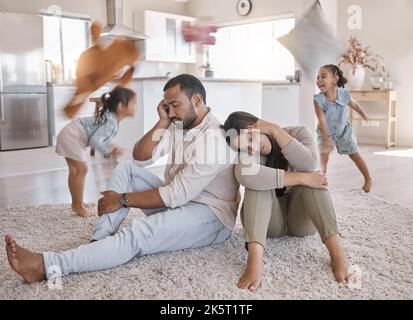A young mixed race couple looking stressed at home while their kids play around them, Hispanic mother and father lacking energy as their kids play in Stock Photo