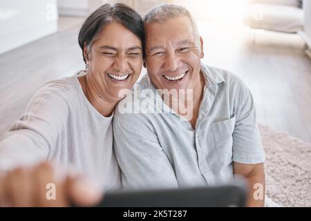 Closeup of an affectionate senior couple taking selfies while relaxing in the living room at home. Mixed race couple having fun taking photos in the Stock Photo