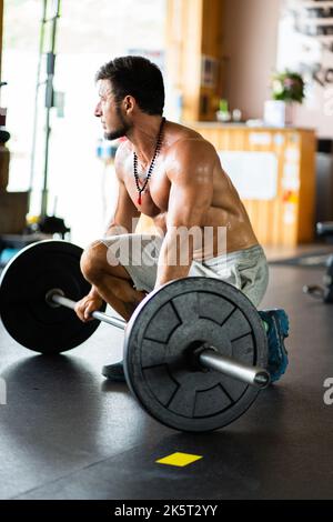 Man resting in a gym while holding a bar with weights Stock Photo