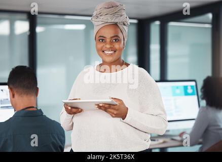 Portrait of confident young african american businesswoman browsing on a digital tablet device while working in an office with her colleagues in the Stock Photo