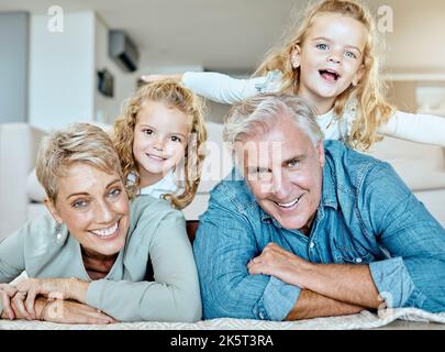 Portrait of two little girls spending time with their grandparents on the lounge floor at home . Mature caucasian couple having fun with their Stock Photo