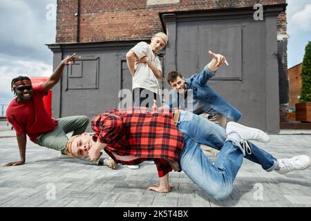 Motion shot of young man doing handstand poses outdoors with all male breakdance team in background Stock Photo