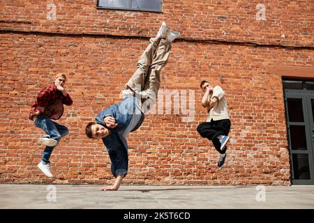 Freeze frame of all male breakdancing team jumping in air and posing against brick wall Stock Photo