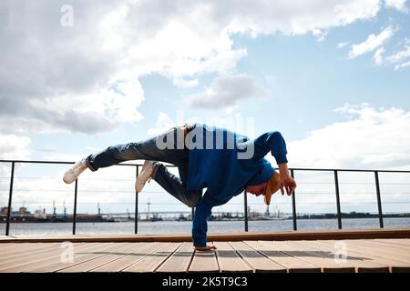 Motion shot of young man doing breakdance handstand pose against sky outdoors, copy space Stock Photo