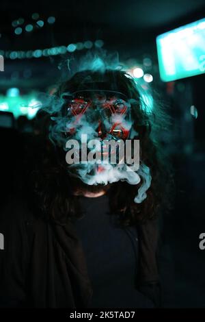 Man in hood with long disheveled hair in a lighting neon glowing mask. Stock Photo
