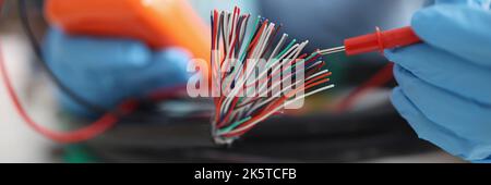 Hands with a voltmeter check colored wires in the cable, blurry Stock Photo
