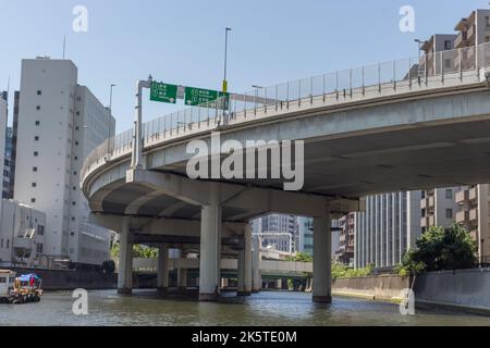 Elevated expressway roads and buildings, viewed from below, from the Sumida river, Tokyo, Japan. The green signs show destinations in both English and Stock Photo