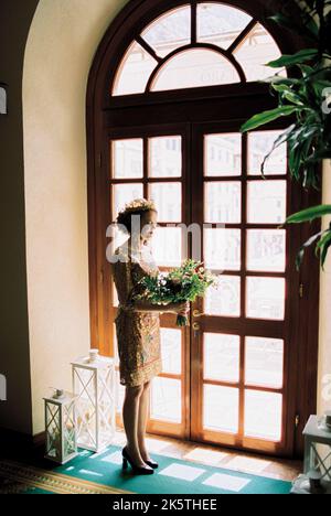 Bride with a bouquet in her hands stands near the arched glass door Stock Photo