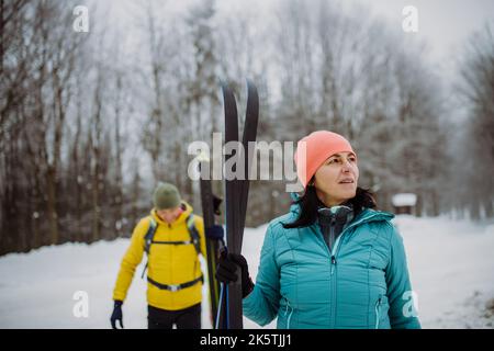 Senior couple crossing forest with skis in hands. Stock Photo