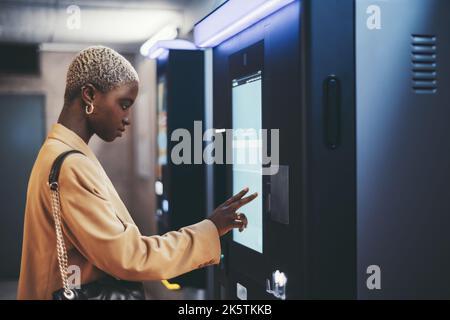 A side view of a young beautiful elegant black woman with painted white very short hair paying for service underground parking or buying a subway or t Stock Photo