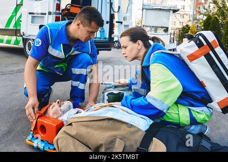 Paramedics immobilized senior patient with neck brace and spinal board to prevent damage in case of spinal injury. First aid from ambulance technician Stock Photo