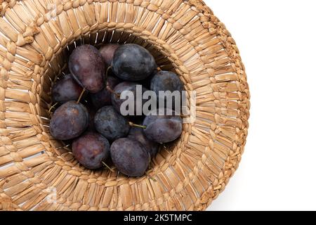 straw hat with plums isolated on white background, fresh fruits close-up Stock Photo