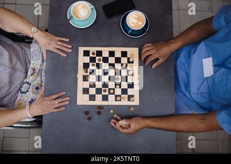 Top view of caregiver playing chess and drinking coffe with his client outdoor at cafe. Stock Photo