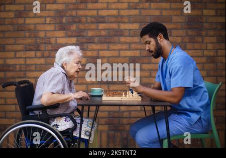 Caregiver playing chess and drinking coffe with his client outdoor at cafe. Stock Photo