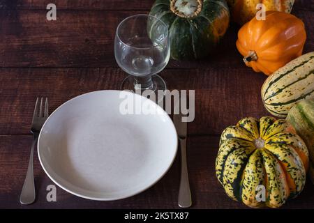 An autumn harvest of squash and a plate with flatware and a glass ready for a meal to be served. Stock Photo