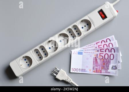 Euro banknotes with power plug of an extension socket on gray surface. Concept for the rising cost of electricity. Expensive energy bill and rising el Stock Photo