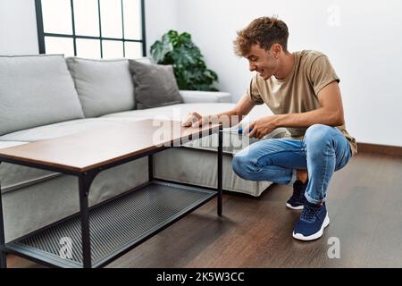 Young caucasian man smiling confident repairing table using screwdriver at home Stock Photo