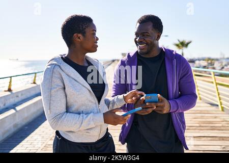 Man and woman couple wearing sportswear using smartphone at seaside Stock Photo