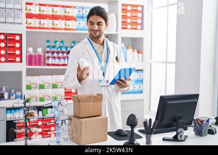Young hispanic man pharmacist using touchpad holding pills bottle at pharmacy Stock Photo
