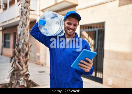 Young hispanic man courier holding water bottle using touchpad at street Stock Photo