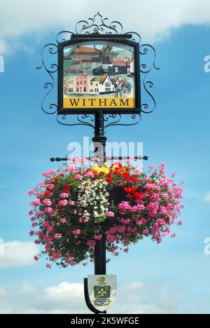 Witham town centre Newland Street sign depicting historical features with colourful summer flowers in hanging basket floral display Essex England UK Stock Photo