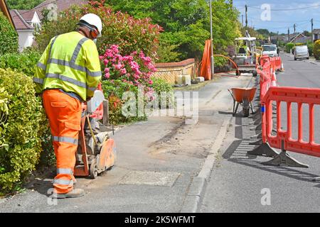 Health & safety kit worn by road works construction site worker using disc saw cutting machine new underground broadband cable infrastructure site UK Stock Photo