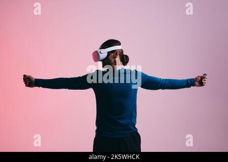 Young man playing a virtual reality shooting game. Young man standing with his arms outstretched while wearing a virtual reality headset. Man explorin Stock Photo