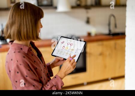 Woman controls home devices with a digital tablet at home Stock Photo
