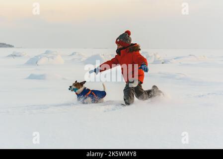 On pleasant winter day kid chasing family pet dog in deep snow Stock Photo