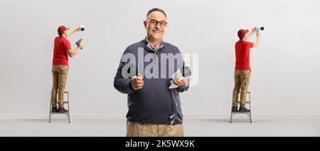 Workers installing security cameras on a wall and mature man posing with a camera in his hands Stock Photo