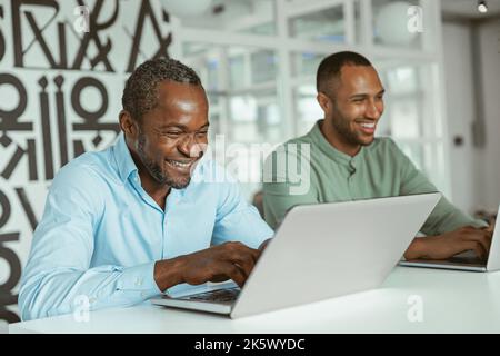 Smiling african businessman working on laptop sitting in coworking on colleagues background Stock Photo