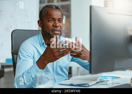 Busy african businessman making videocall to client while sitting in modern office Stock Photo