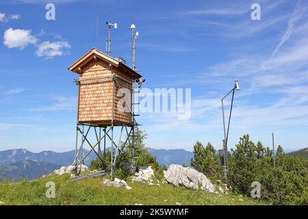 Mountain top meteorological (weather) station on a small cabin with a blue sky, mountains, and scattered clouds Stock Photo