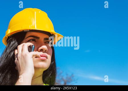 closeup of young latin caucasian venezuelan woman. wearing yellow safety helmet talking on the phone frowning and confused, technology concept, copy s Stock Photo