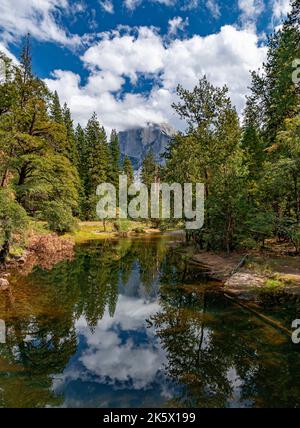 Clouds partially fill a blue sky over the Merced River while El Capitan looms in the distance, Yosemite National Park, California Stock Photo