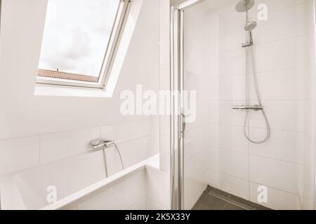 Clean bathtub located near shower box with glass door in modern bathroom with white tiled walls Stock Photo