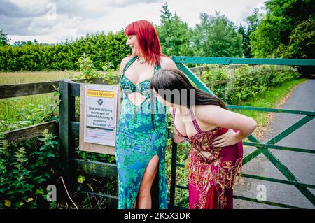 Two belly dancers wearing dress costume examine a sign warning about anti-social activity in a rural area. Stock Photo