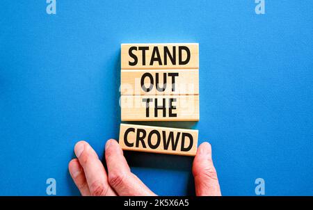 Stand out the crowd symbol. Concept words Stand out the crowd on wooden blocks on beautiful blue table blue background. Businessman hand. Business, st Stock Photo